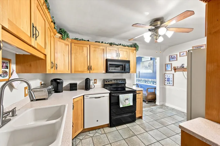 Kitchen featuring wood cabinetry, a dual-basin sink with a gooseneck faucet, a black range with an overhead microwave, and a ceiling fan with light fixture