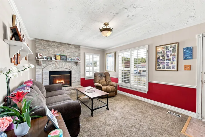Brick fireplace with an arched firebox, carpeted flooring, and crown molding
