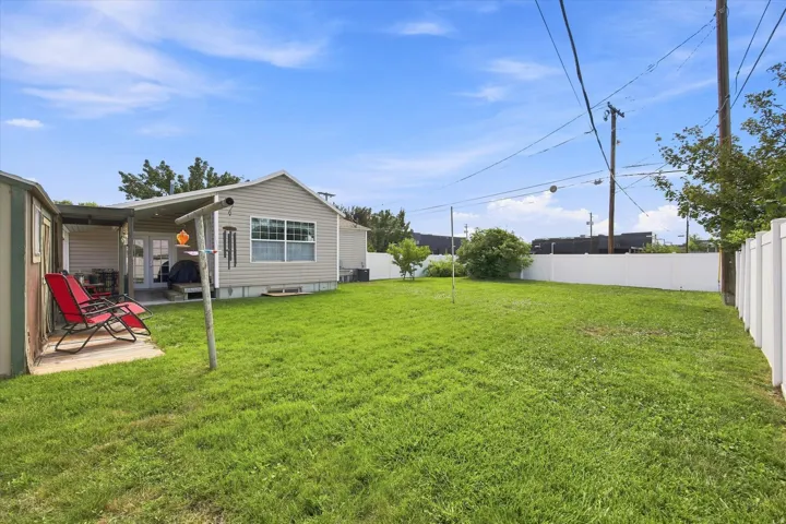 Expansive backyard featuring a large grassy area, white privacy fencing, and a covered back patio with French doors
