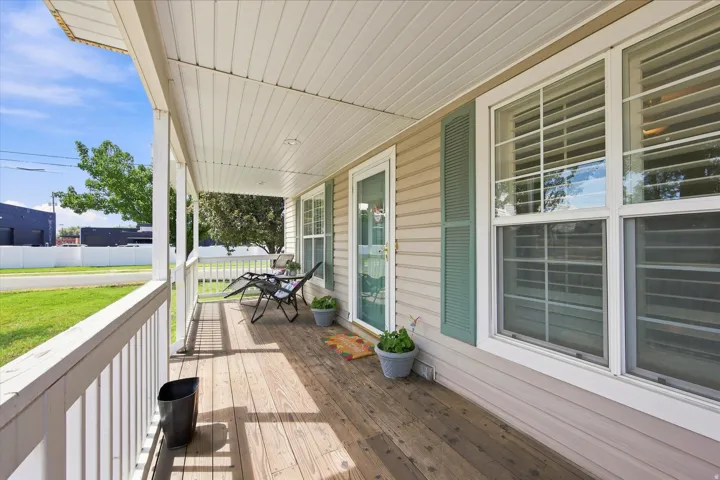 Covered front porch with wood-finish flooring, white railing, and vinyl siding