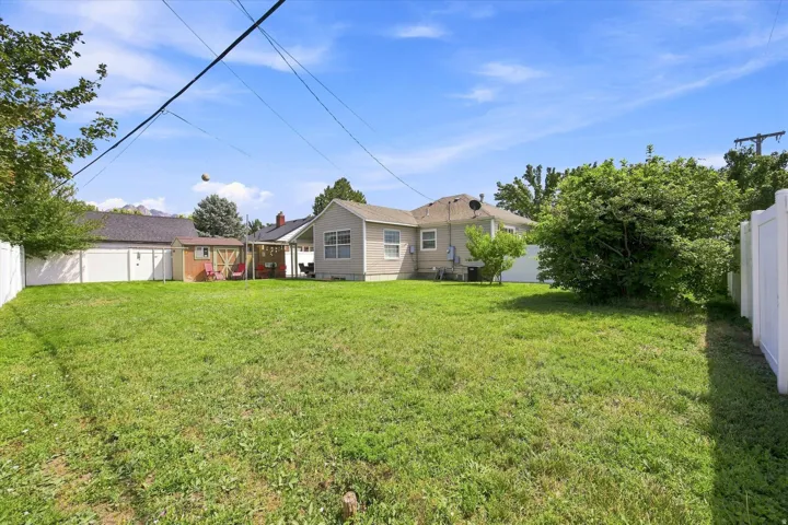 Expansive lawn area with white vinyl fencing, a detached shed, and a covered patio structure