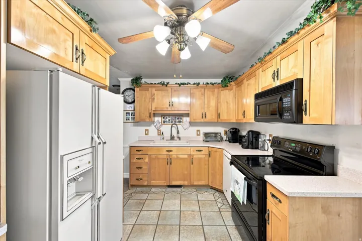 Wood-finish cabinetry, tile flooring, ceiling fan with integrated lighting, and black appliances