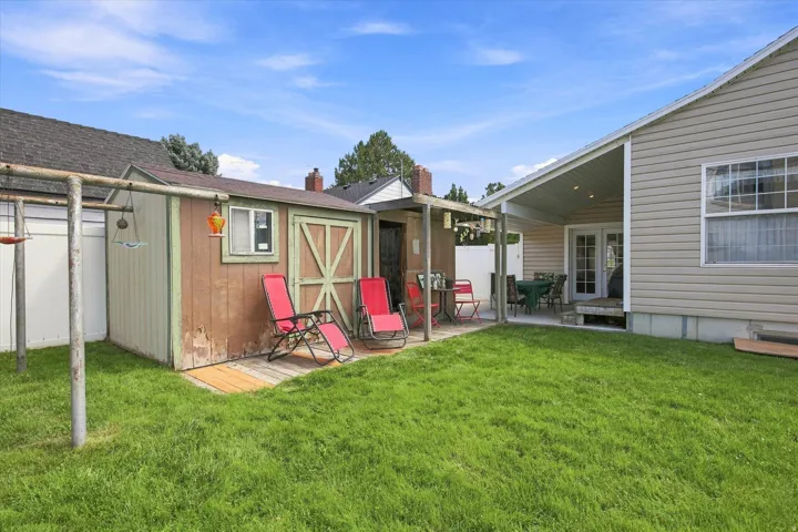 Expansive grassy yard with a storage shed, concrete patio, and a covered back porch with a ceiling fan