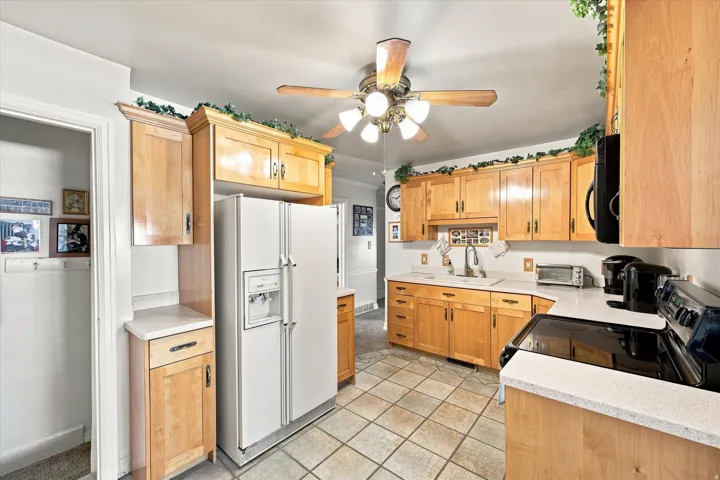 Wood-finish cabinetry paired with white countertops, a ceiling fan, and tile flooring