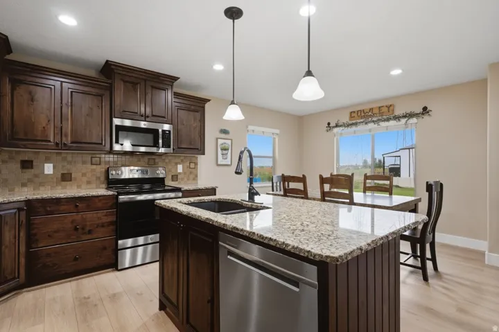 Kitchen featuring wood-finish flooring, dark wood cabinetry, stainless steel appliances, speckled countertops, and a tile backsplash