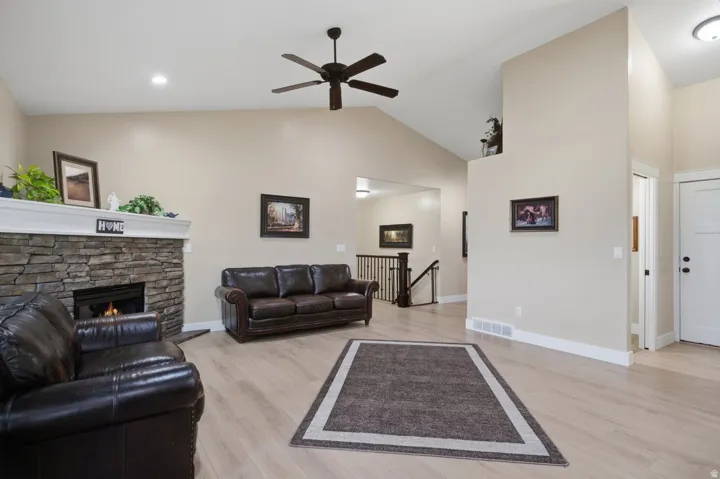Vaulted ceilings with a ceiling fan, stone-clad fireplace, wood-finish flooring, and a staircase with dark wood railings