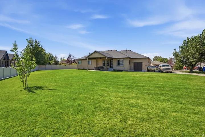 Expansive rear lawn, covered patio, privacy fencing, attached garage, and mature landscaping