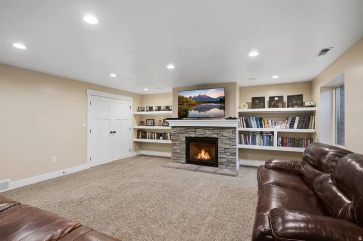 Stone-clad fireplace with mantel, recessed lighting, built-in shelving, carpet flooring, and a white paneled double door