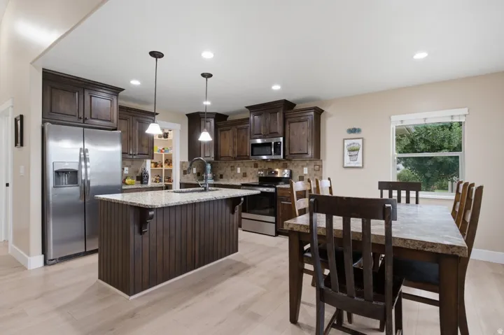 Kitchen featuring dark wood-finish cabinetry, stainless steel appliances, a center island with pendant lighting, and light-tone wood-finish flooring
