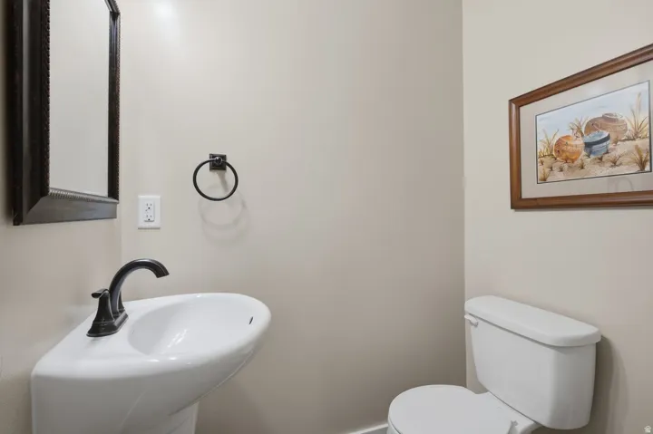 Pedestal sink with dark-finished faucet, wall-mounted mirror, and white toilet