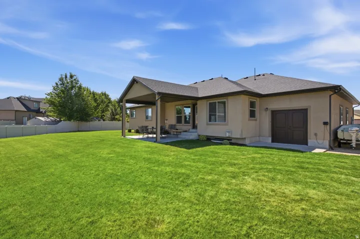 Expansive green lawn, covered patio, stucco exterior, asphalt shingle roof, and a two-door utility access