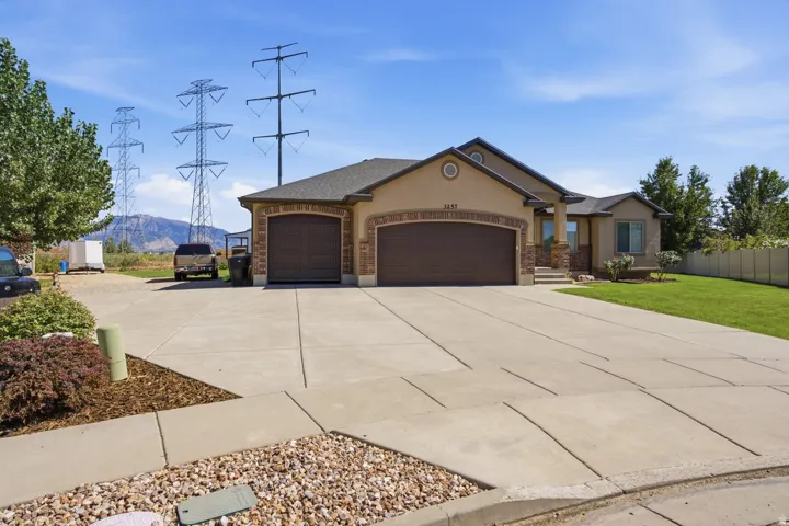 Stucco exterior with stone accents, two-car garage, concrete driveway, and manicured lawn