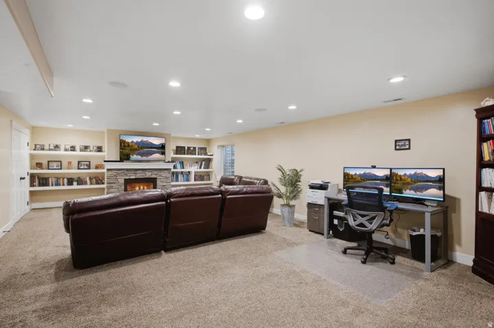 Recessed lighting, stone-clad fireplace, integrated shelving, built-in desk area, and carpeted flooring