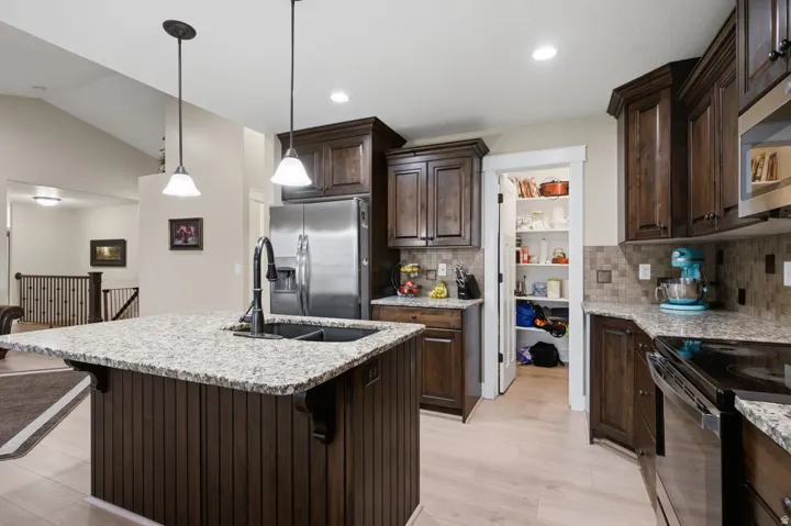 Chef's kitchen featuring dark wood cabinetry, white quartz countertops, a large center island with pendant lighting, stainless steel appliances, and light wood-finish flooring throughout the open-concept space