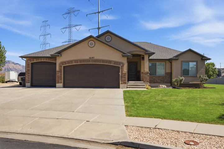 Stucco exterior with brick accents, attached three-car garage, concrete driveway, front yard with lawn, and a covered entry
