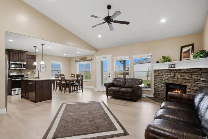 Vaulted ceilings, a stone-faced fireplace, light wood-finish flooring, dark wood cabinetry, and stainless steel appliances