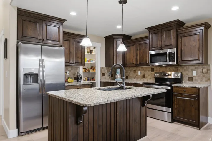 Kitchen featuring dark wood cabinetry, stainless steel appliances, granite countertops, and a tiled backsplash