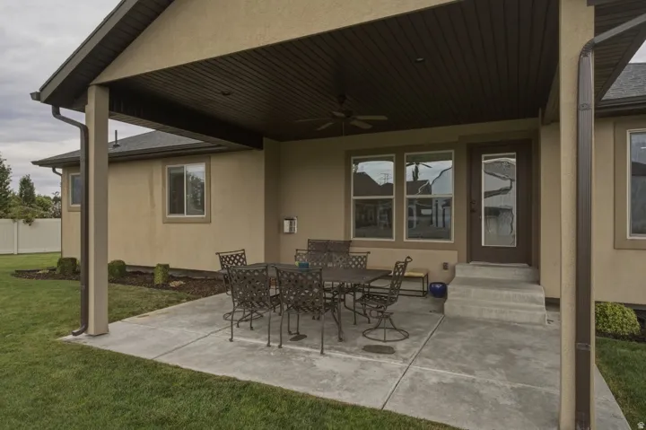 Covered concrete patio with a ceiling fan, direct exterior access, and surrounding lawn
