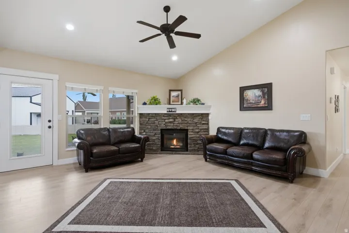 Vaulted ceiling with a ceiling fan, stone-clad fireplace, wood-finish flooring, recessed lighting, and large windows