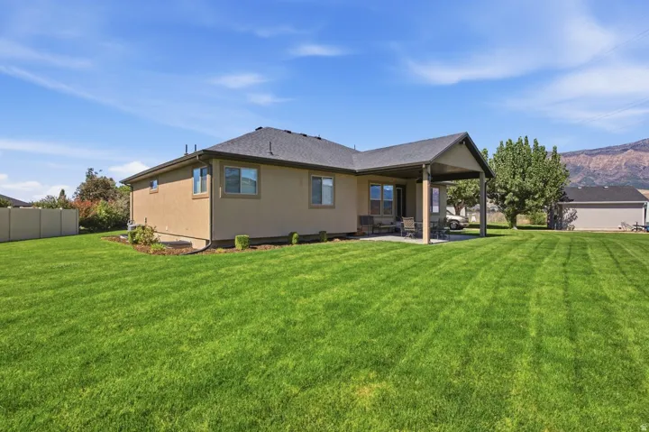 Expansive green lawn, covered patio, stucco exterior, privacy fence, and mountain backdrop