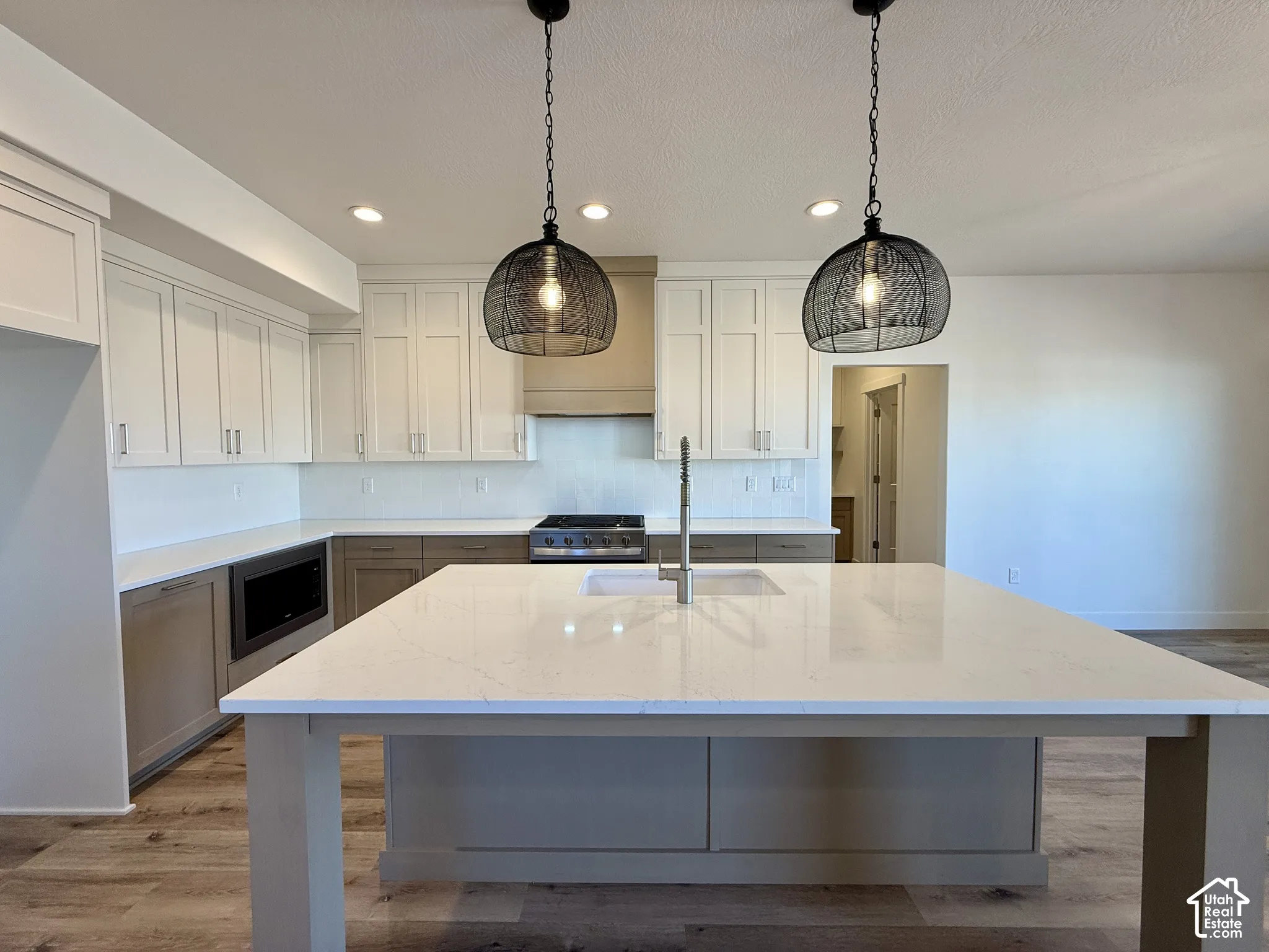 Kitchen featuring a large central island with a quartz countertop, two-toned cabinetry, stainless steel range, recessed lighting, and dual pendant light fixtures