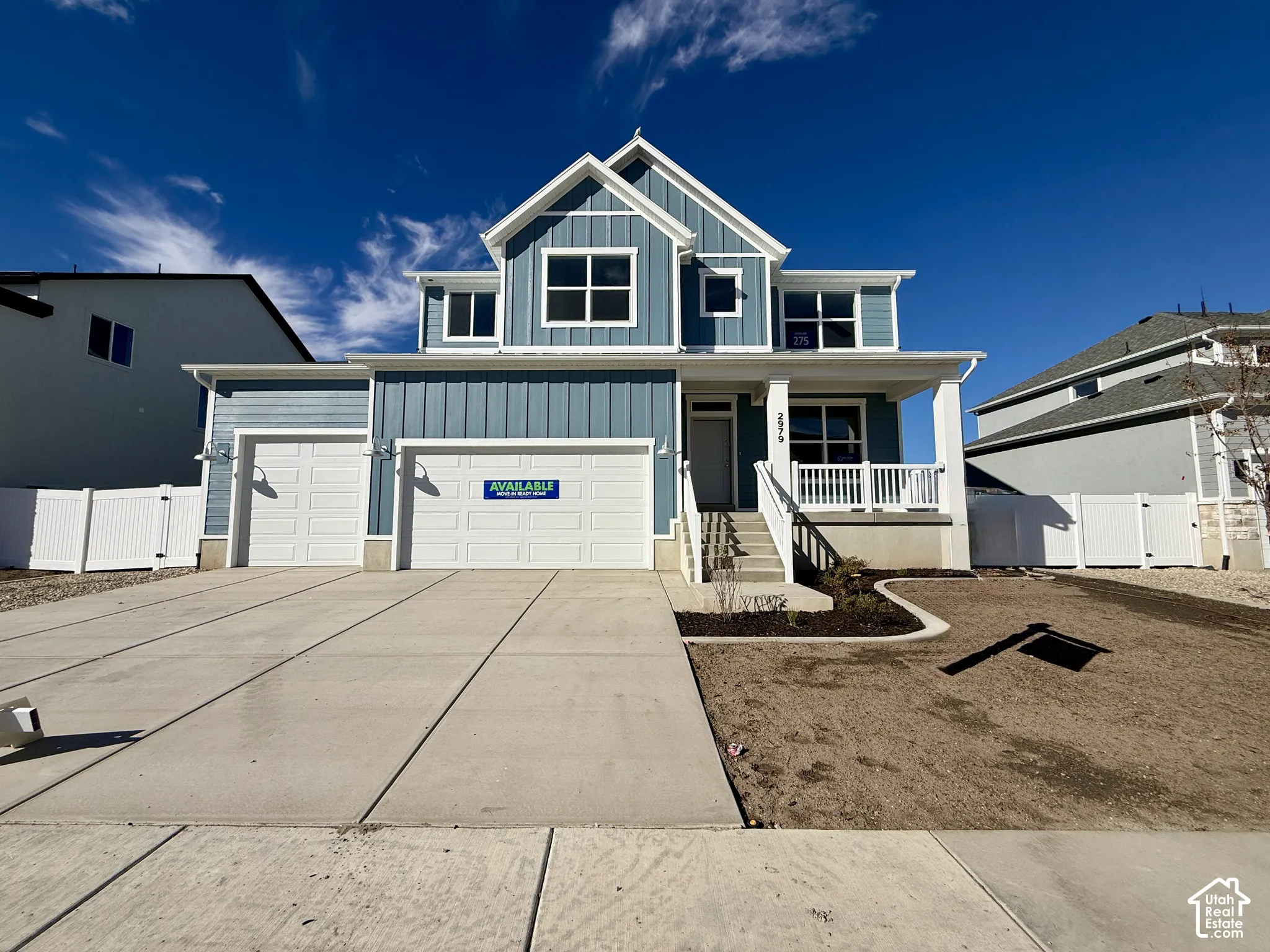 Blue board-and-batten exterior with a two-car garage, covered front porch, and white vinyl privacy fencing