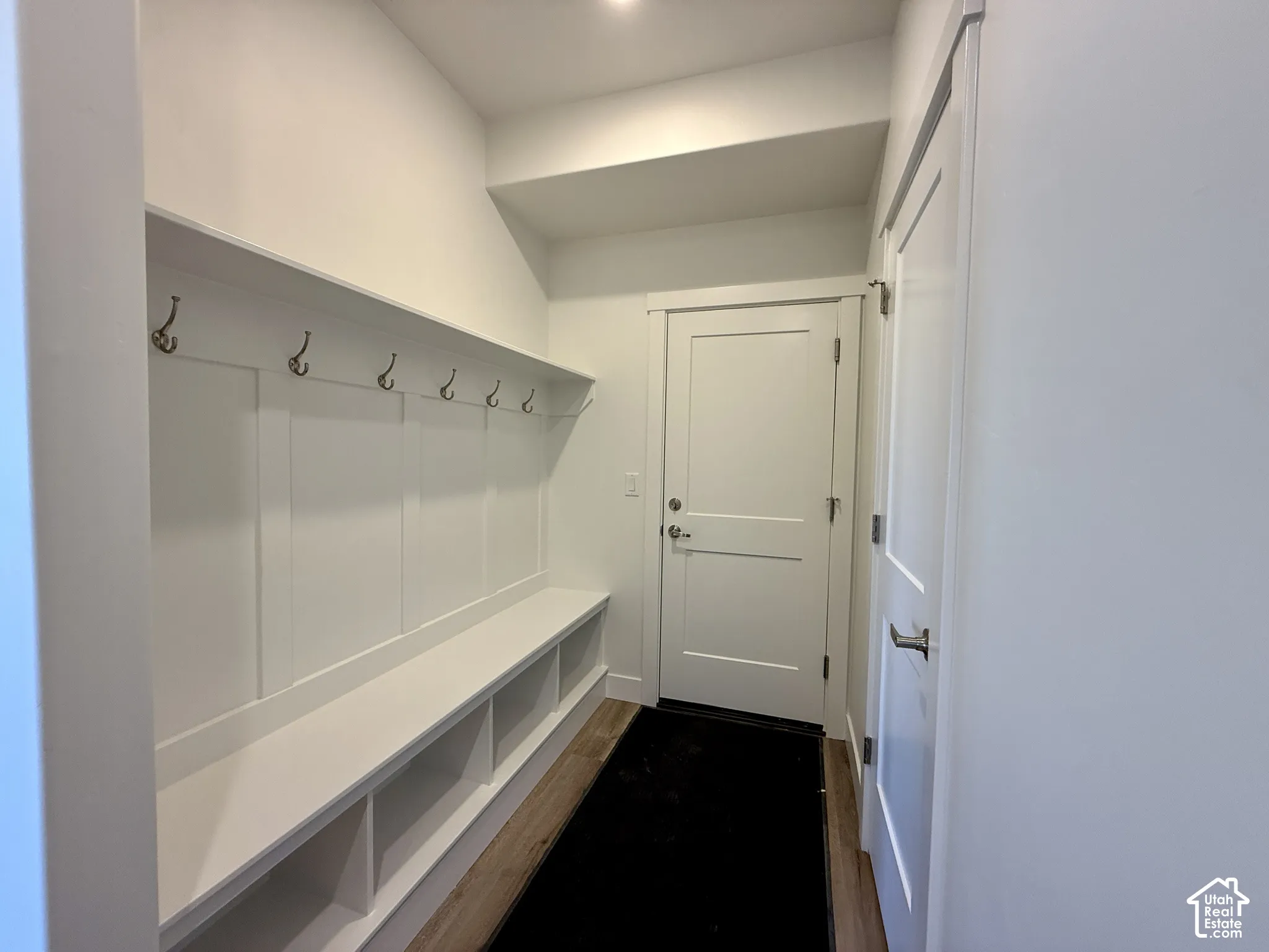 Built-in mudroom cabinetry featuring integrated storage cubbies, a bench, wall-mounted hardware, and panel-style wainscoting with wood-finish flooring