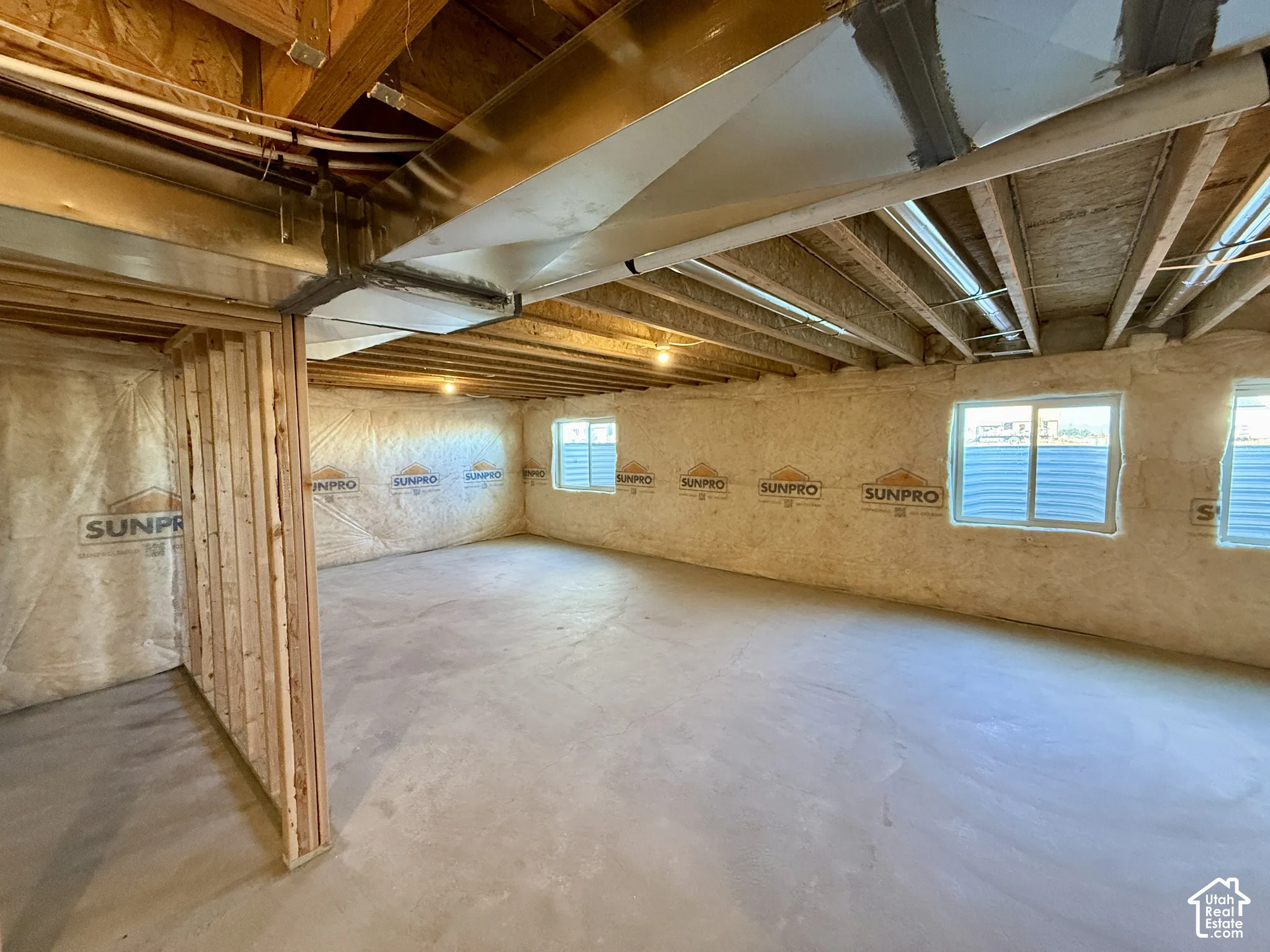 Unfinished interior space featuring exposed wood joists, concrete flooring, spray foam wall insulation, and multiple egress windows
