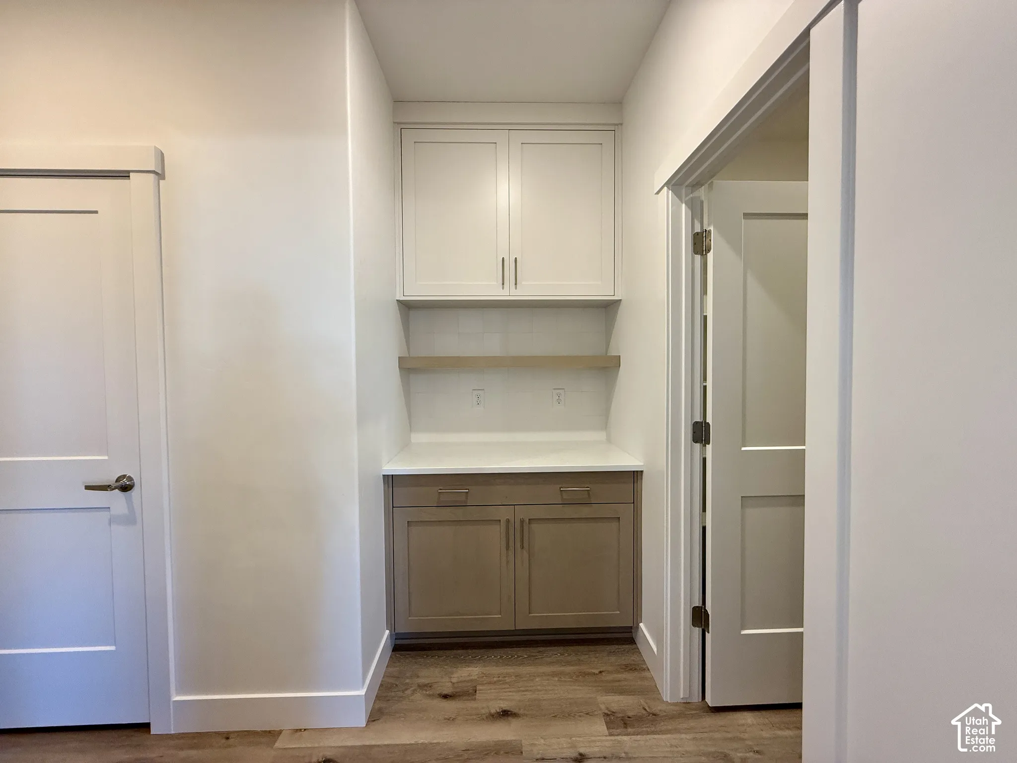 Built-in cabinetry featuring upper white cabinets, lower wood-finish cabinets, a solid surface countertop, a floating shelf, and wood-finish flooring