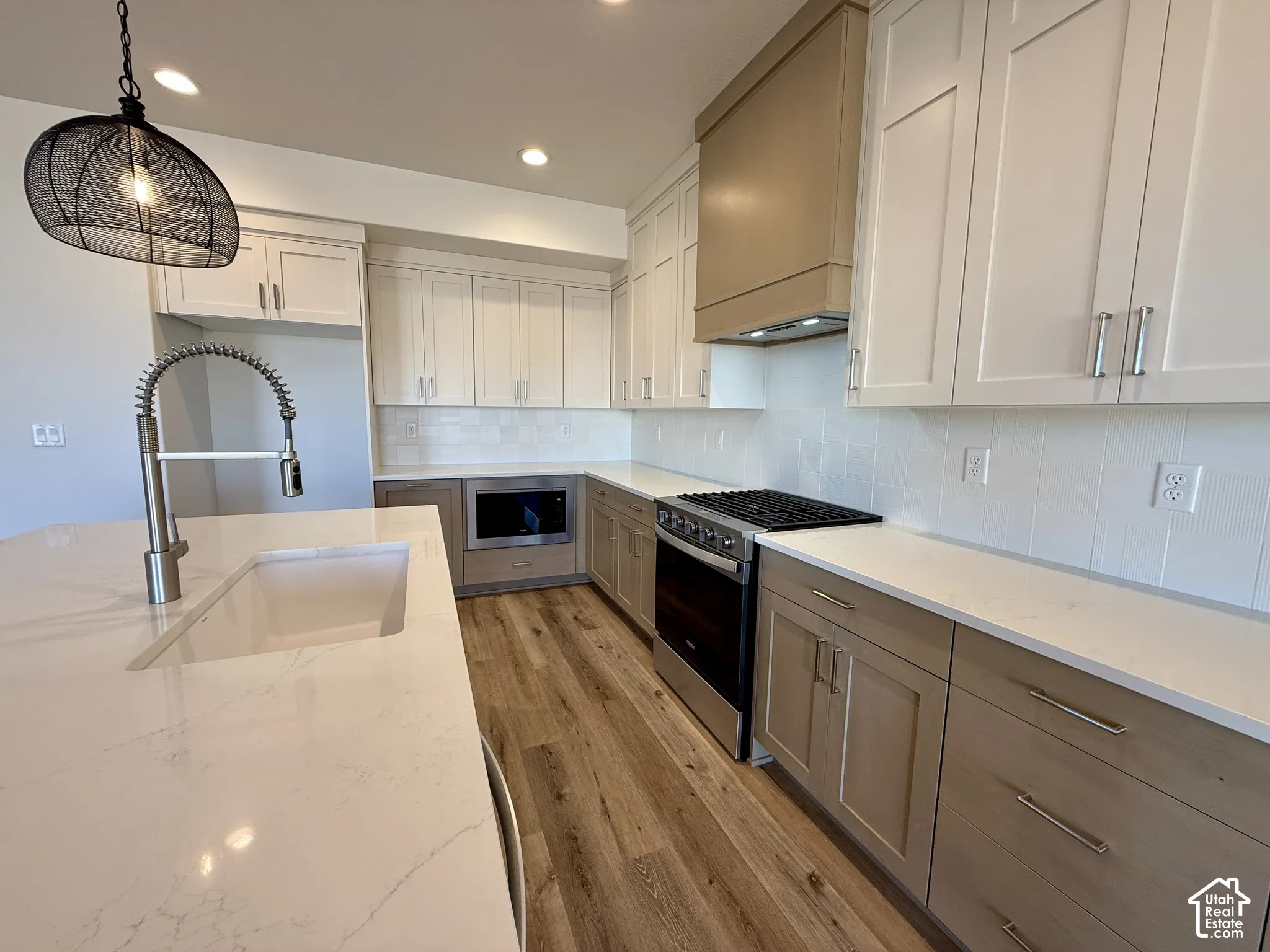 Kitchen featuring custom cabinetry with mixed finishes, quartz countertops, a farmhouse-style sink with a pull-down faucet, stainless steel appliances, and wood-finish flooring