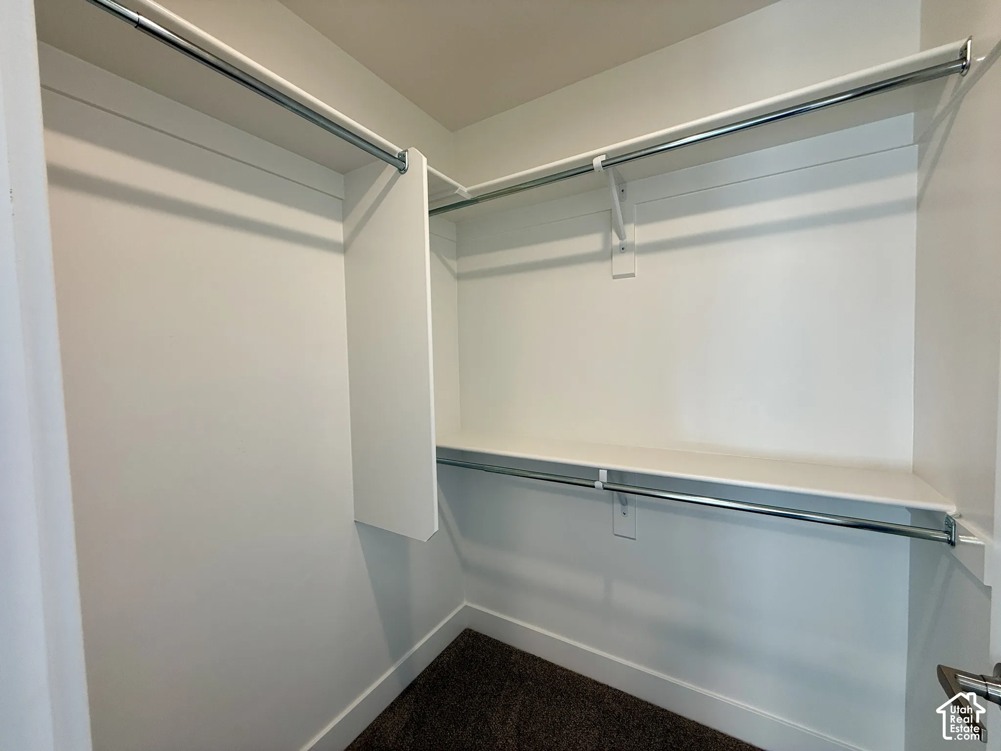 Walk-in storage space featuring multi-level metal hanging rods and white shelving