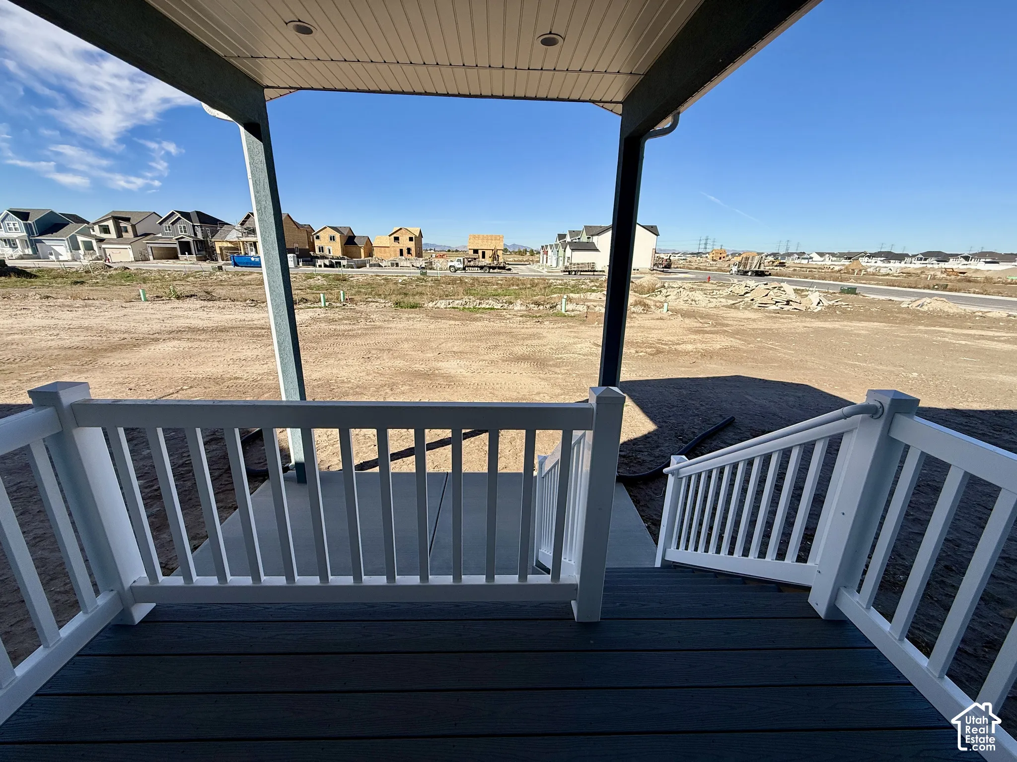 Covered outdoor deck with white vinyl railing, recessed ceiling lighting, and concrete stair landing