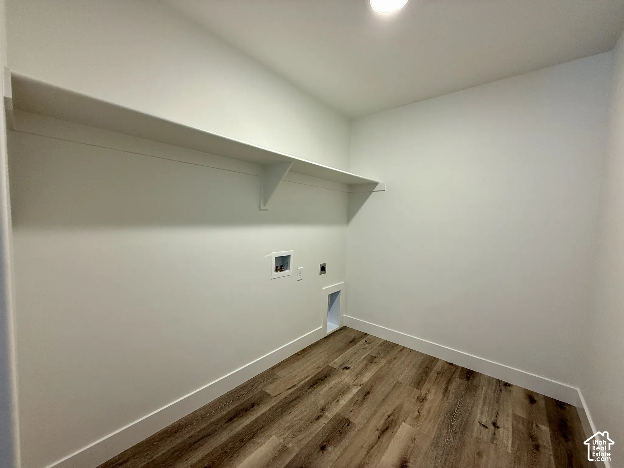 Utility area featuring wood-finish flooring, a built-in overhead shelf, and designated laundry hookups