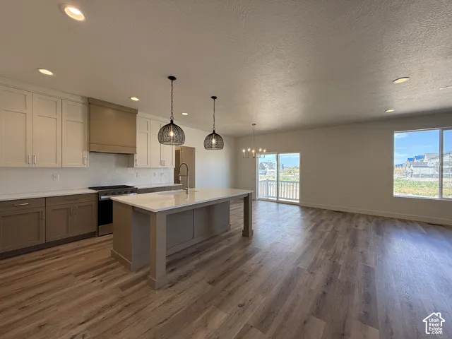 Open-concept living space featuring wood-finish flooring, a kitchen island with stone countertop, stainless steel appliances, and abundant natural light from large windows and a sliding glass door