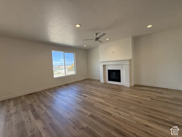 Spacious living area featuring wood-finish flooring, a decorative fireplace with a mantel, a ceiling fan, and recessed lighting