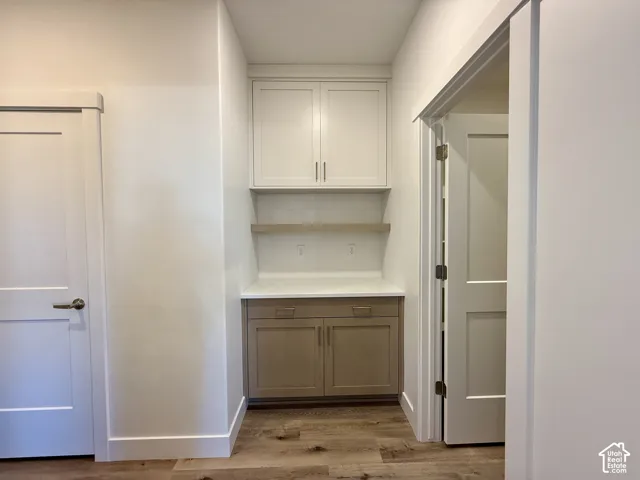 Built-in cabinetry featuring upper white cabinets, lower wood-finish cabinets, a solid surface countertop, a floating shelf, and wood-finish flooring
