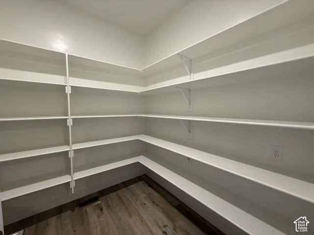 Walk-in pantry featuring expansive white shelving and wood-finish flooring