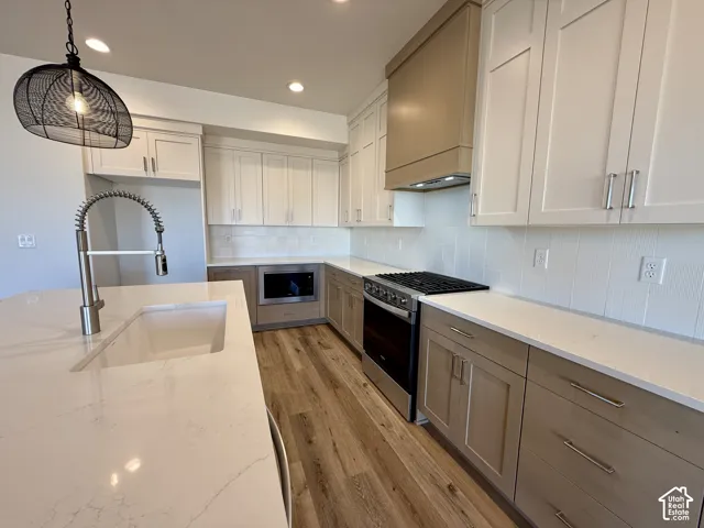 Kitchen featuring custom cabinetry with mixed finishes, quartz countertops, a farmhouse-style sink with a pull-down faucet, stainless steel appliances, and wood-finish flooring
