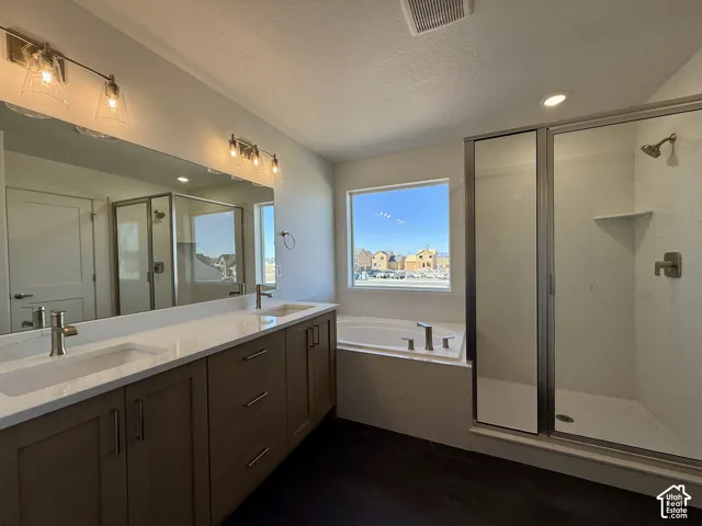 Double vanity featuring solid-surface countertops, undermount sinks, contemporary light fixtures, soaking tub with deck-mounted faucet, and a glass-enclosed shower with a metallic finish showerhead