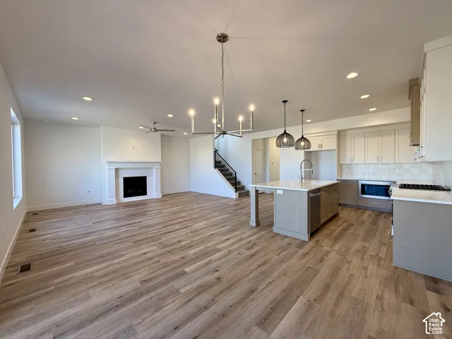 Wood-finish flooring, fireplace with a decorative mantel, center kitchen island with integrated sink, two-tone cabinetry, and multi-light chandelier