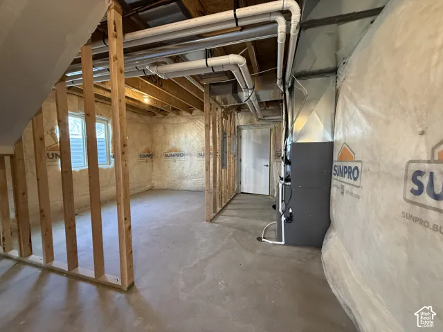 Unfinished basement featuring exposed wood framing, concrete flooring, visible HVAC system, and a window