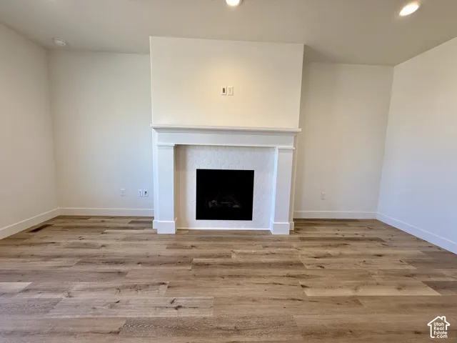 Fireplace featuring a classic white mantle, hexagonal tile surround, wood-finish flooring, and recessed ceiling lighting