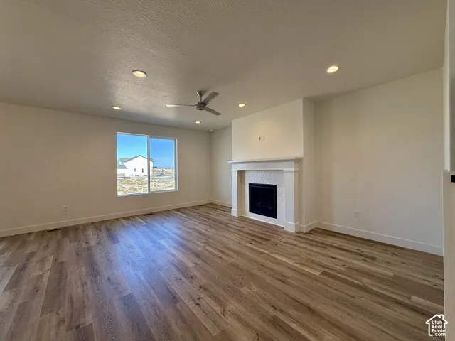 Living area featuring wood-finish flooring, recessed lighting, a ceiling fan, and a fireplace with a decorative mantel surround