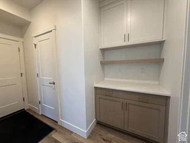 Built-in cabinetry with white upper cabinets and lower wood-finish cabinets, white countertop, wood-finish floating shelf, and white tile backsplash