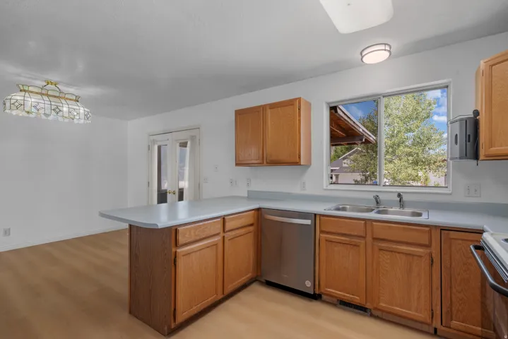 Kitchen featuring wood-finish cabinetry, light-toned countertops, and a stainless steel dishwasher