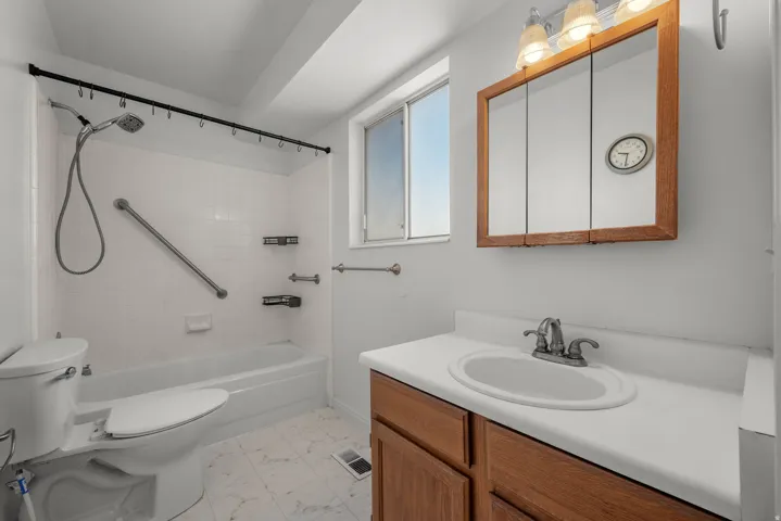 White bathtub with a shower head and tiled surround, complete with a grab bar