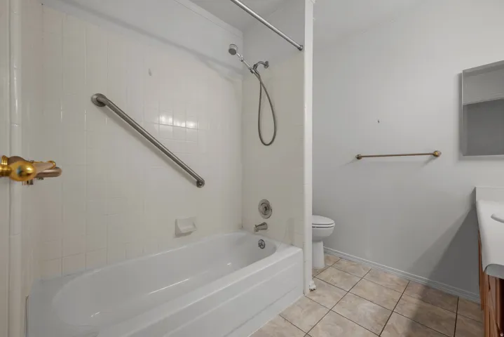 White tiled shower-tub combination with grab bar