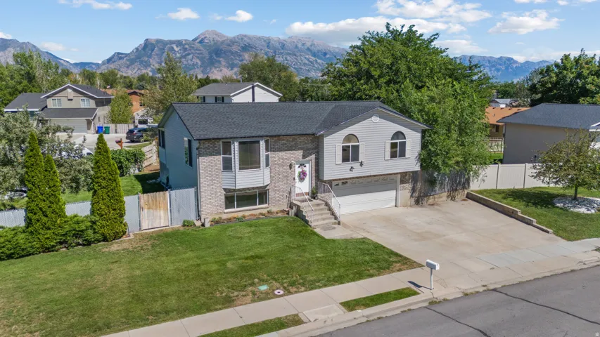 Split-level residence featuring a brick and siding exterior, an attached garage, a paved driveway, and a front lawn with established landscaping