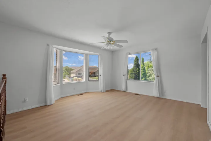 Light-toned wood-finish flooring, bay window with a wide sill, ceiling fan, and white walls