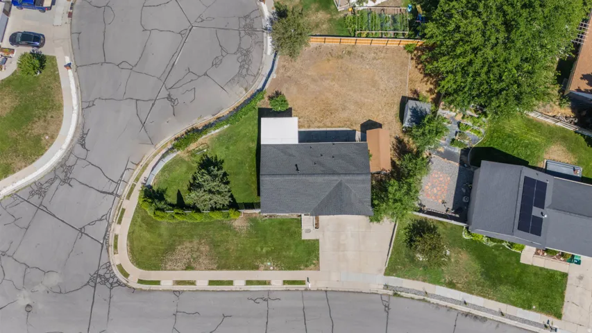Shingled roof, paved driveway, mature trees, manicured lawn, and a fenced backyard